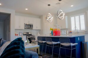 A modern kitchen with white cabinets, a central island, bar stools, and pendant lighting.