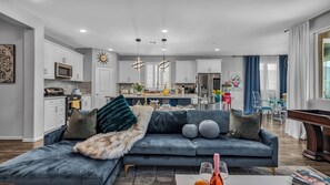 A modern living room with a grey sectional sofa, a fluffy throw blanket, and a coffee table with a bottle and glasses.