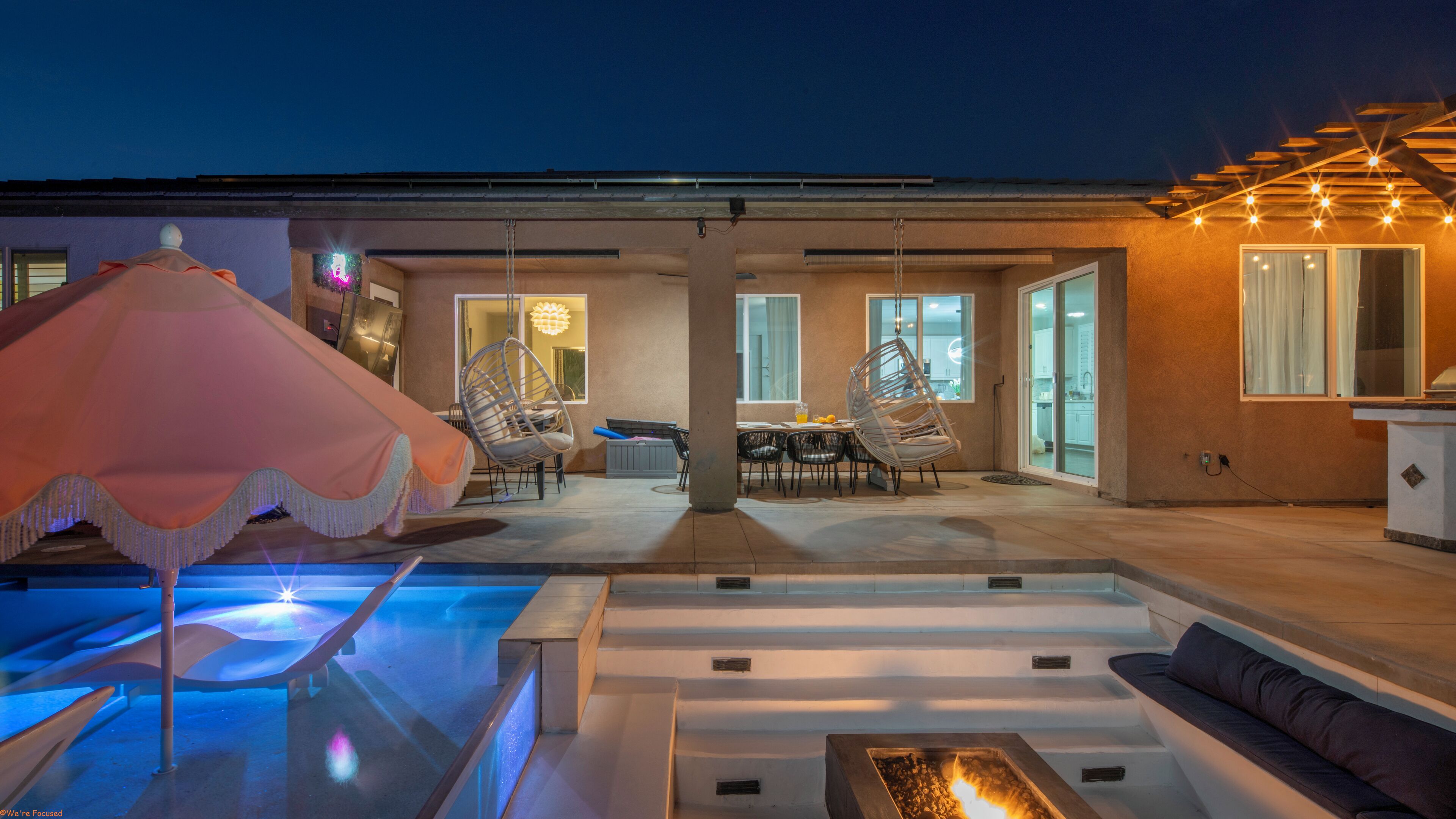 An outdoor pool area with a seating area, a hanging chair, and a pergola with lights.