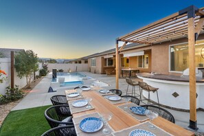 A backyard with a pool, dining area, barbecue, and a pergola.