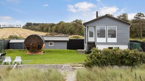 Ein modernes Haus mit einem großen, fassförmigen Bau im Garten, einem kleinen Gästehaus und einem gepflegten Rasen.