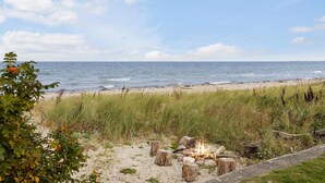 Ein Strand mit Feuerschale und Holzbalken, umgeben von Gras und Pflanzen.