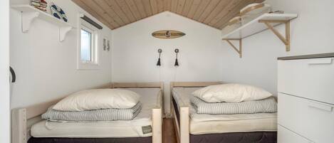 A compact bedroom with two single beds, wooden ceiling beams, white walls, and built-in storage shelves.