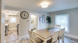 A dining area with a wooden table, four chairs, a clock, and framed pictures on the wall. - Coastal Comfort & Golfers' Paradise in Sheboygan! (Sheboygan)