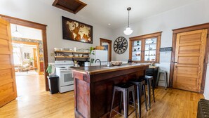 A kitchen with a wooden island, bar stools, a large clock, and a world map on the wall. - Our Place Inn Munising; Munising | 5 Min to Pictured Rocks | 3BR (Munising)