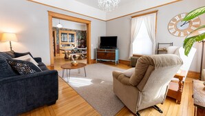 A living room with a sofa, armchair, TV, and a wooden floor. - Our Place Inn Munising; Munising | 5 Min to Pictured Rocks | 3BR (Munising)