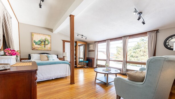 A bedroom with a bed, a chair, a table, and large windows. - Our Place Inn Munising; Munising | 5 Min to Pictured Rocks | 3BR (Munising)