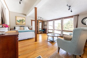 Un dormitorio con una cama, una silla, una mesa y ventanas amplias.