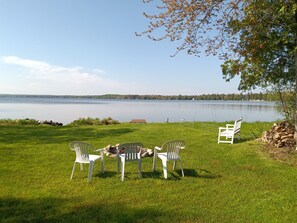 Une zone herbeuse avec des chaises en plastique blanches et un banc, le tout donnant sur un lac paisible.