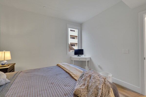 A bedroom with a bed, a bedside table with a lamp, a TV on a small table, and a window with a view of a building.