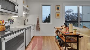 A modern kitchen with white cabinets, a microwave, and a wooden countertop. There is a window with a view of trees and a door to the right. - The Bish: Traverse City Fall Getaway | Wine Country & Downtown | Sleeps 2 (Traverse City)