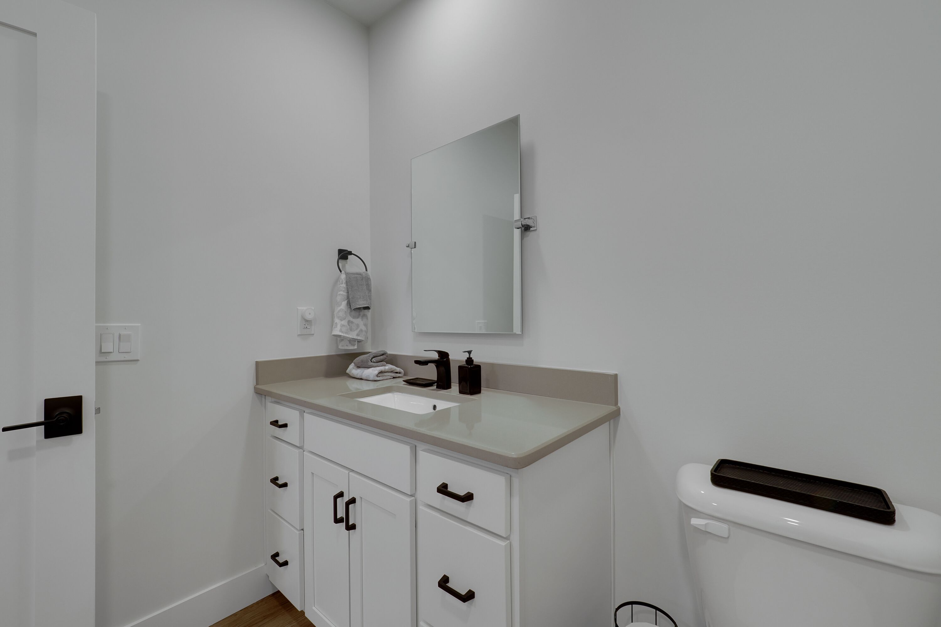 Un baño con lavamanos blanco, espejo y retrete. Hay una toalla colgada en la pared y un cubo de basura pequeño junto al retrete.
