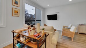 A modern living room with a sofa, a coffee table, a television, and a wicker chair. - The Bish: Traverse City Fall Getaway | Wine Country & Downtown | Sleeps 2 (Traverse City)
