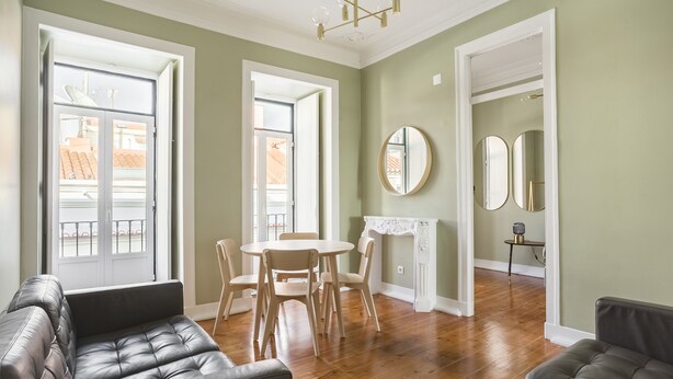 Un vaste salon doté d’un plancher en bois, un coin repas avec une table ronde et des chaises, et une cheminée avec un manteau de couleur blanche.