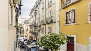 Une ruelle étroite pavée, bordée de voitures garées et d’immeubles dotés de balcons.