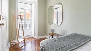 Une chambre à coucher avec un lit, un porte-manteau en bois, un miroir rond et une petite table avec une lampe.