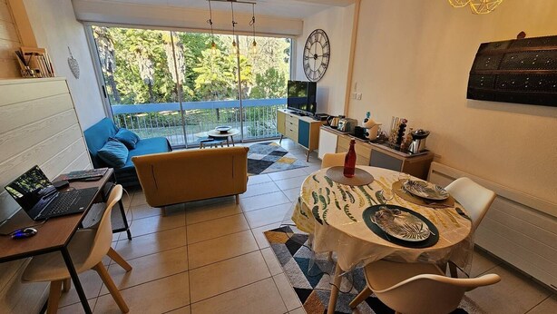 A modern kitchen with a dining area, a sofa, and a TV in the background.