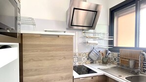 A compact kitchen with wooden cabinets, a microwave, a stainless steel range hood, and a window providing natural light.