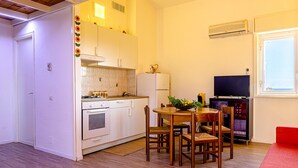 A compact kitchen with white cabinets, a stove, and a dining area with a table and chairs. - Calarosa- Holiday home Giardini Naxos (Giardini Naxos)