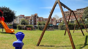 A playground with slides and swings, surrounded by a grassy area and buildings in the background. - Calarosa- Holiday home Giardini Naxos (Giardini Naxos)