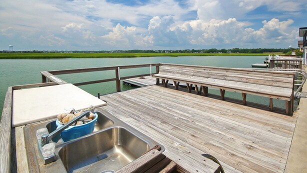 A wooden dock with a metal sink and a blue bucket, overlooking a calm body of water and a green landscape. - Amazing view and we love dogs (North Myrtle Beach)