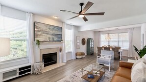 Una sala de estar moderna con chimenea, ventilador de techo y un gran ventanal con cortinas.