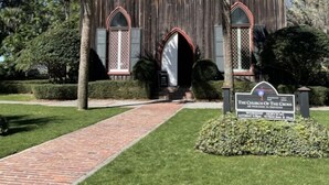 Una iglesia de madera con un sendero de ladrillo que conduce a la entrada, rodeada de palmeras y follaje cuidado.