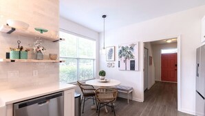 Una cocina moderna con lavavajillas, un comedor con sillas de mimbre y una puerta roja al fondo.