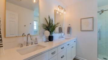 A modern bathroom with a large mirror, two sinks, and a shower area.