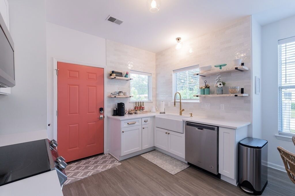 A compact kitchen with white cabinets, a red door, and a dishwasher.
