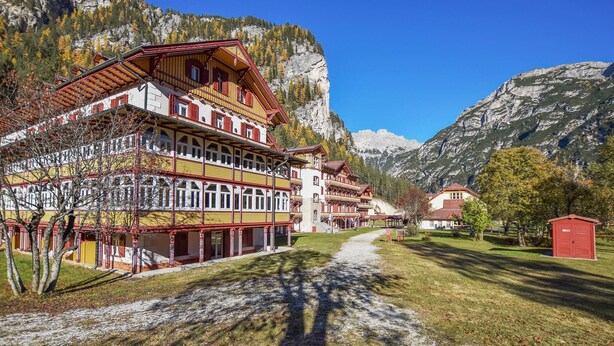 A traditional multi-story building with a red and yellow facade, set against a mountainous backdrop.