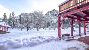 A snow-covered outdoor area with a red wooden structure, possibly a gazebo, and a bench.
