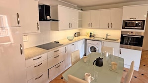 Eine moderne Küche mit weißen Schränken, einem Glastisch und Edelstahlgeräten, darunter eine Spülmaschine, ein Backofen und eine Mikrowelle.