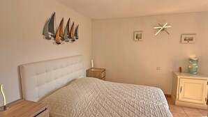 Ein Schlafzimmer mit einem großen Bett, einem Nachttisch, einer Kommode und Wandbildern, darunter Segelboote und eine Uhr.