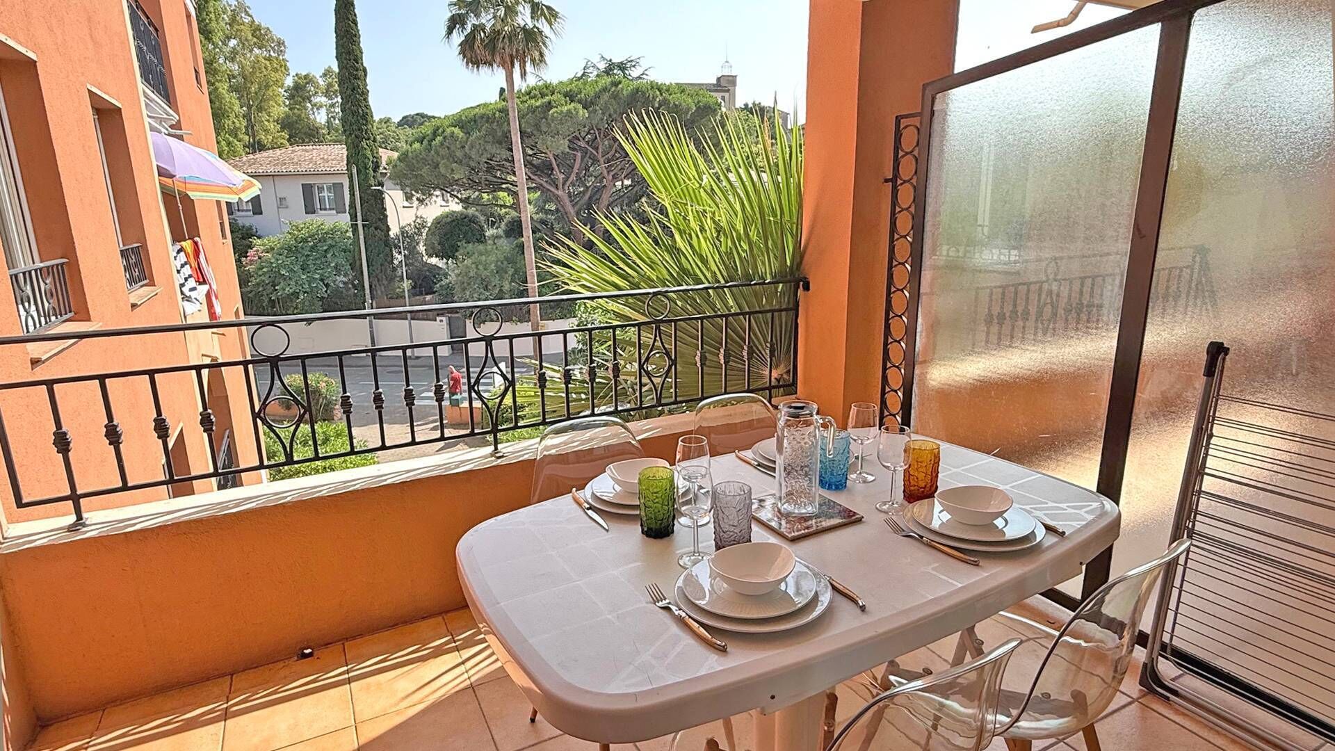 Un balcon avec une table dressée pour le dîner, donnant sur un jardin et des bâtiments.
