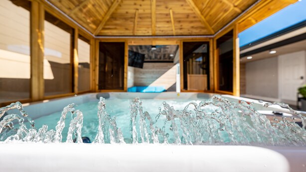 En inredning med träpaneler, ett bubbelbad och utsikt över en pool.