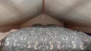 A bedroom with a sloped ceiling, wooden walls, and a patterned bedspread.