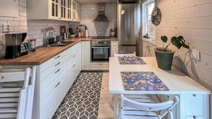 A kitchen with white cabinets, a stainless steel refrigerator, a stove, and a dining table with a patterned table runner.