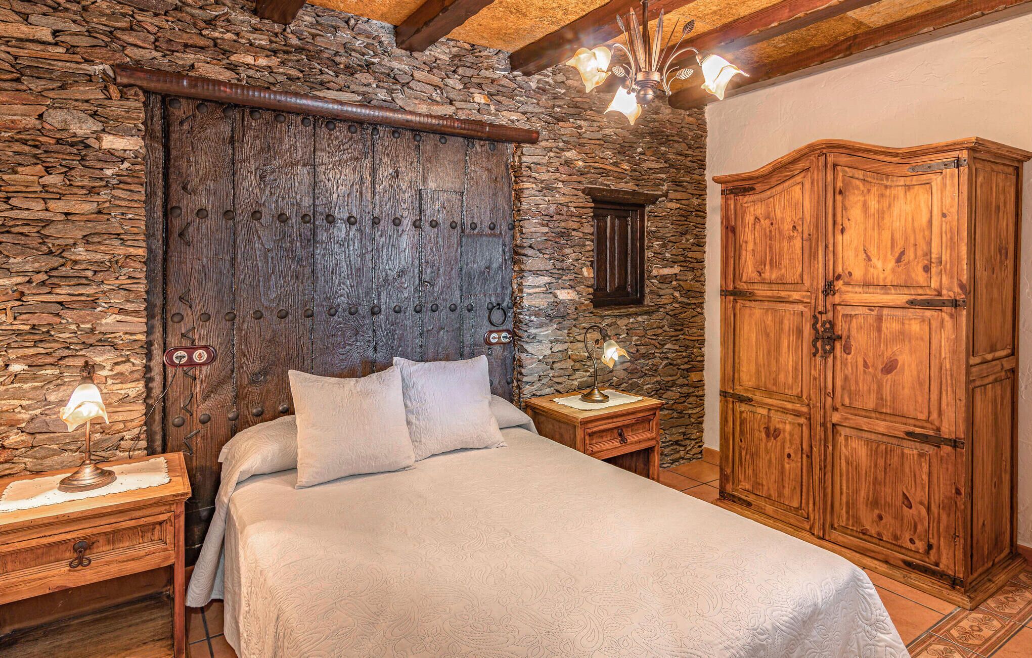 Une chambre avec un mur en pierre, une tête de lit en bois et une armoire en bois.