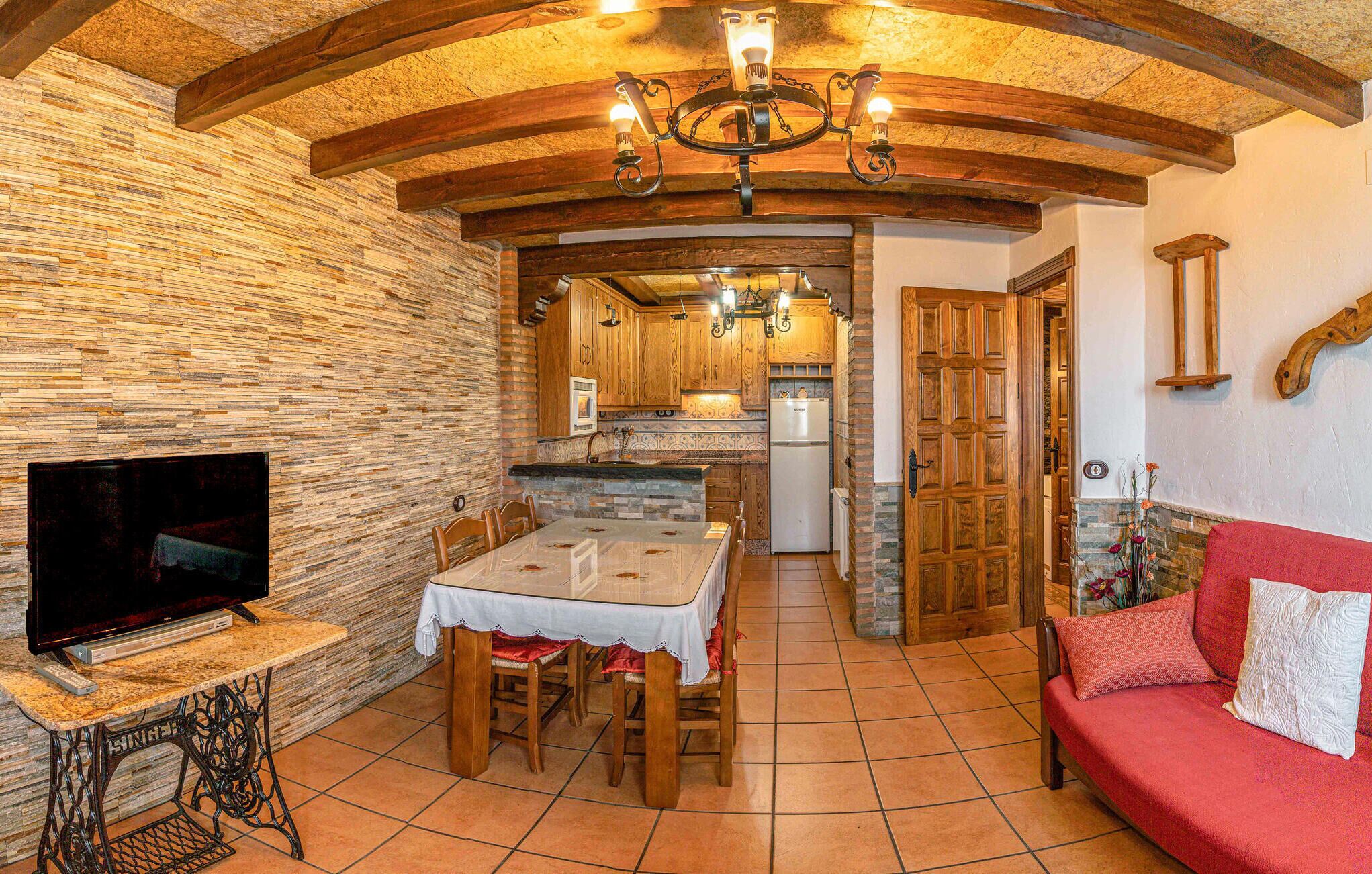 A cozy living room with a TV, a dining area with a table and chairs, and a kitchen with wooden cabinets and a refrigerator.