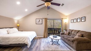 A bedroom with a bed, a ceiling fan, a window with curtains, a sofa, and framed pictures on the wall.
