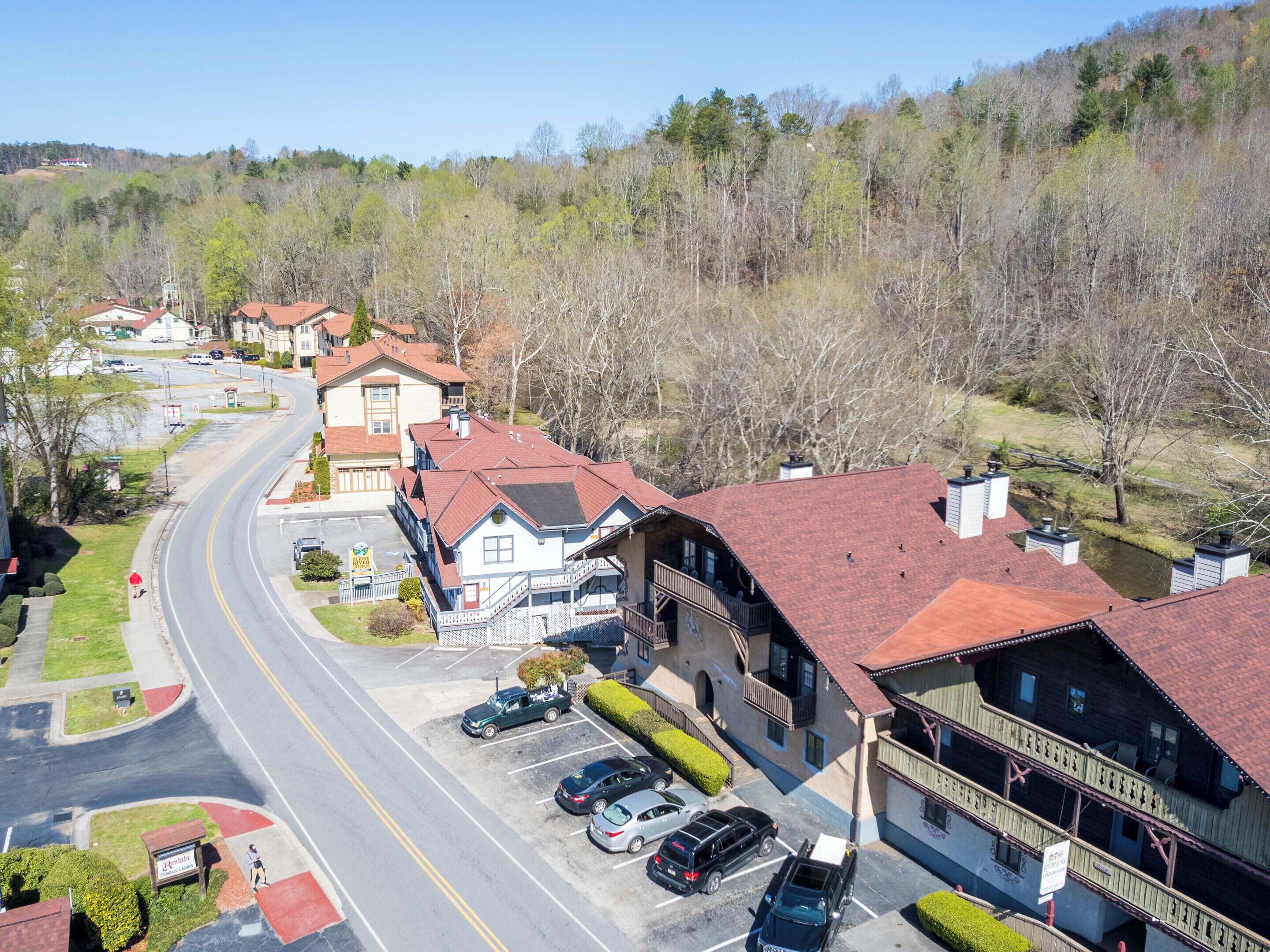 A multi-story building with a red roof, a parking lot with several cars, and a road curving around the property.