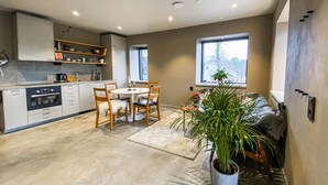 Une cuisine compacte dotée d’appareils électroménagers modernes, un coin repas avec une table ronde et des chaises, et une grande fenêtre laissant entrer la lumière naturelle.
