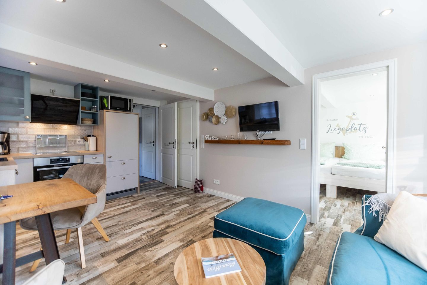Ein zeitgemäßer Wohnraum mit Küche, Essbereich und einer gemütlichen Sitzecke mit Fernseher und Bett.