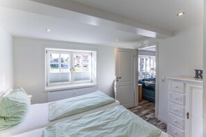 Un dormitorio con cama, ventana, puerta y cómoda.