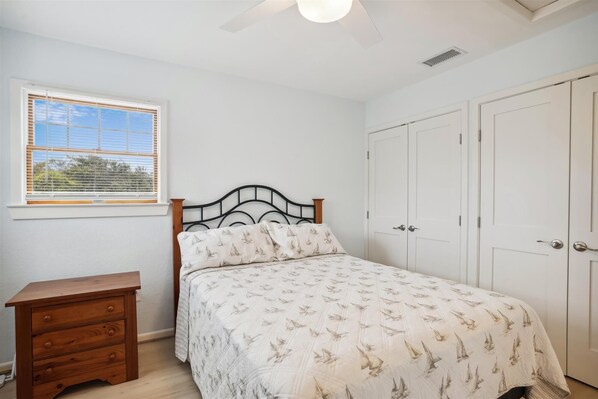 A bedroom with a bed, a nightstand, a window with blinds, and a wardrobe.