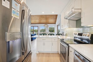 A modern kitchen with stainless steel appliances, white cabinetry, and a view to the outdoors.