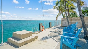 A deck with steps leading to the water, a lifebuoy, and blue chairs. - Oceanfront PARADISE w Heated pool, 55’ dock, ocean view & bathroom in every room (Marathon)