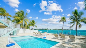 A pool area with a clear view of the ocean, palm trees, and a staircase leading to a building. - Oceanfront PARADISE w Heated pool, 55’ dock, ocean view & bathroom in every room (Marathon)