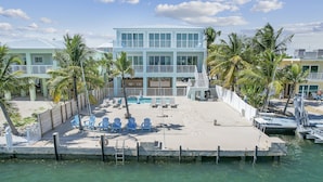 A beachfront property with a pool, lounge chairs, and a dock. - Oceanfront PARADISE w Heated pool, 55’ dock, ocean view & bathroom in every room (Marathon)